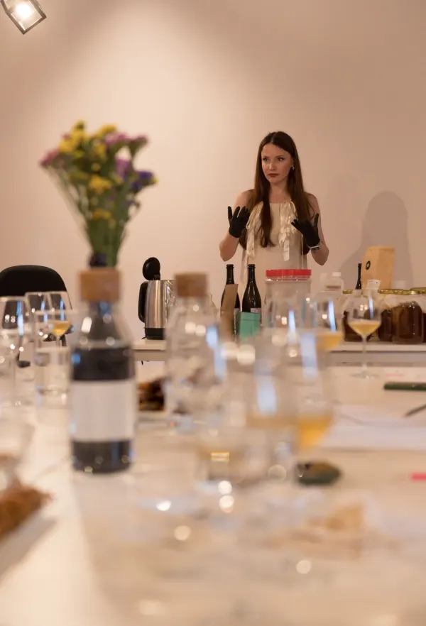 Ioana, cu mănuși negre, explicând procesul de fermentație în spatele unei mese cu sticle, borcane și un fierbător
