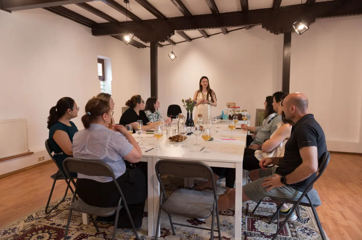 Participanți așezați la o masă lungă albă la Craft Kombucha Workshop, ascultând-o pe Ioana la Common House, București