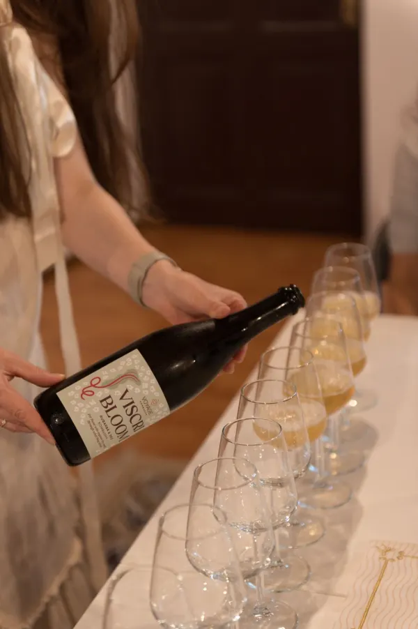 Ioana prezentând o sticlă de kombucha Viscri Bloom lângă un rând de pahare de degustare